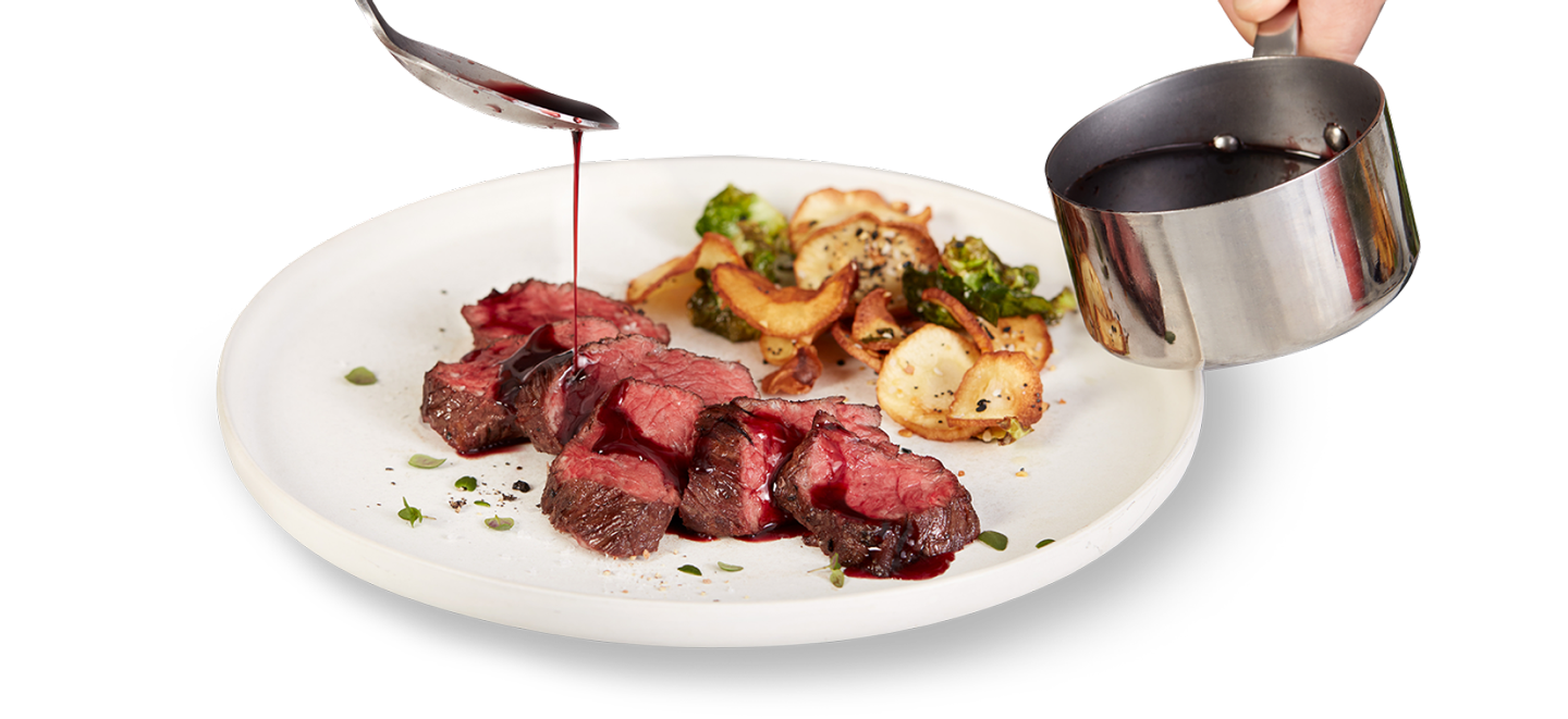 A chef drizzles a red wine reduction over slices of roasted hangar steak