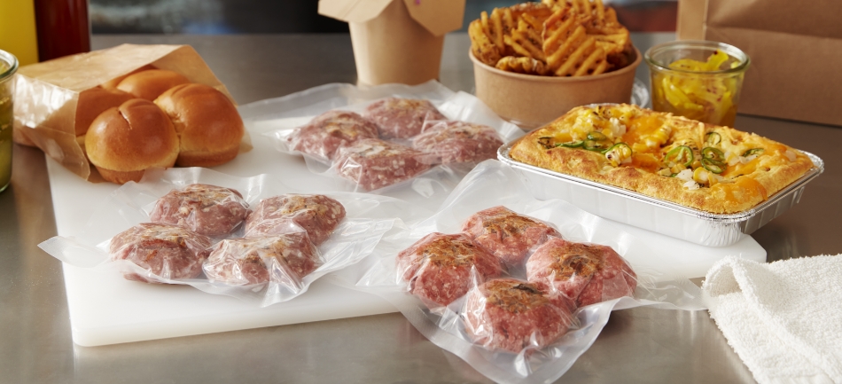 A restaurant meal kit for sliders with vacuum-sealed patties, baked buns, waffle fries and a cheesy jalapeno corn bake