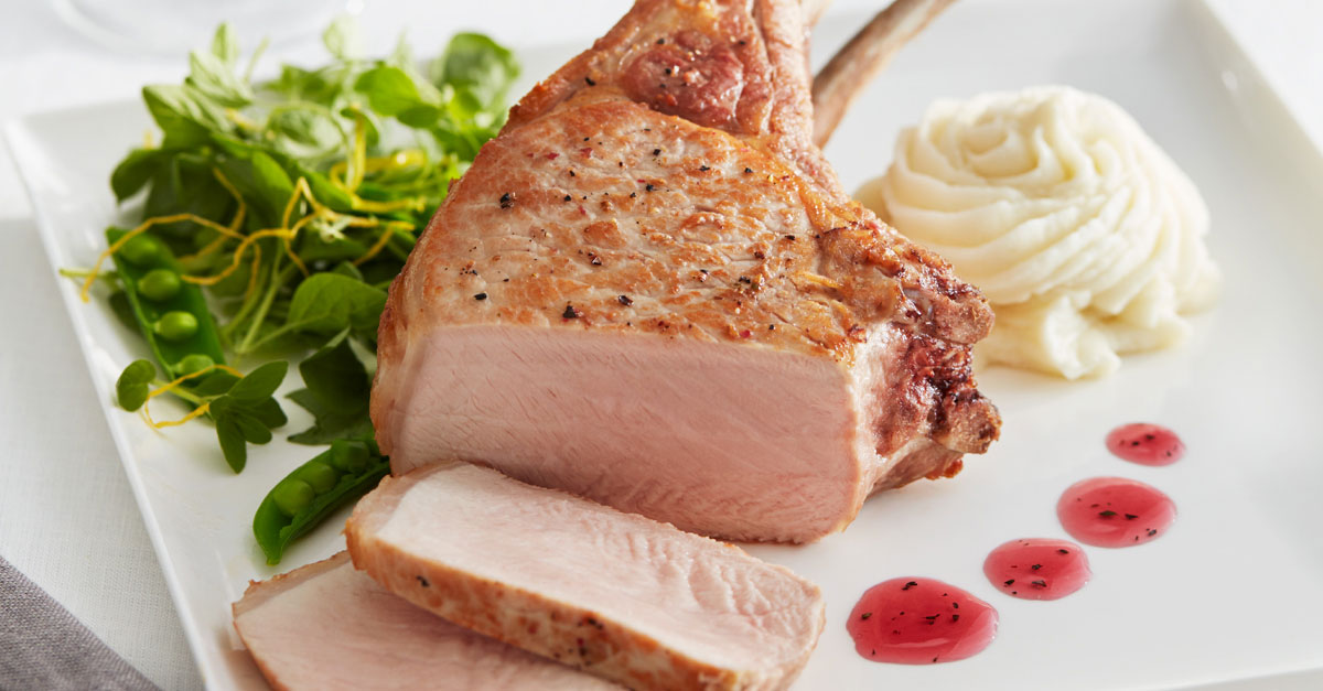 Pink pork chop sliced and served with leafy greens and mashed potatoes